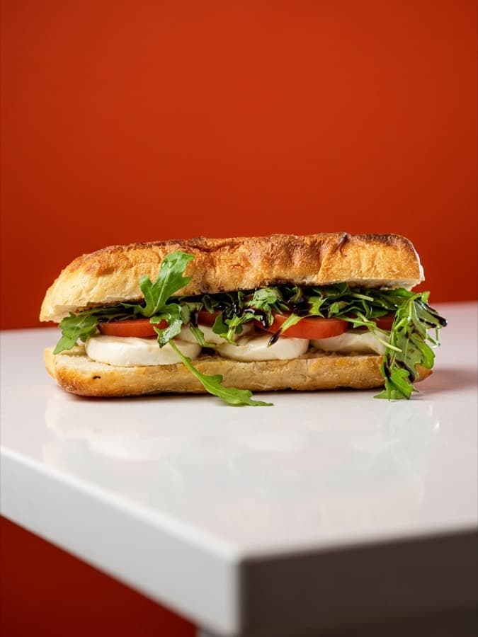 Caprese panino on Pugliese bread with mozzarella, tomato and wild rocket, against a tomato-red wall